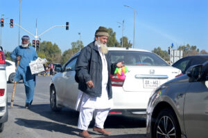 An aged man is selling plastic toys on a busy road.