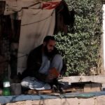 A cobbler is sitting under a tree Polishing a shoes