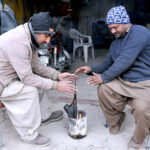 Mechanics sit around the fire to warm their hands as the temperature drops due to rain in the city