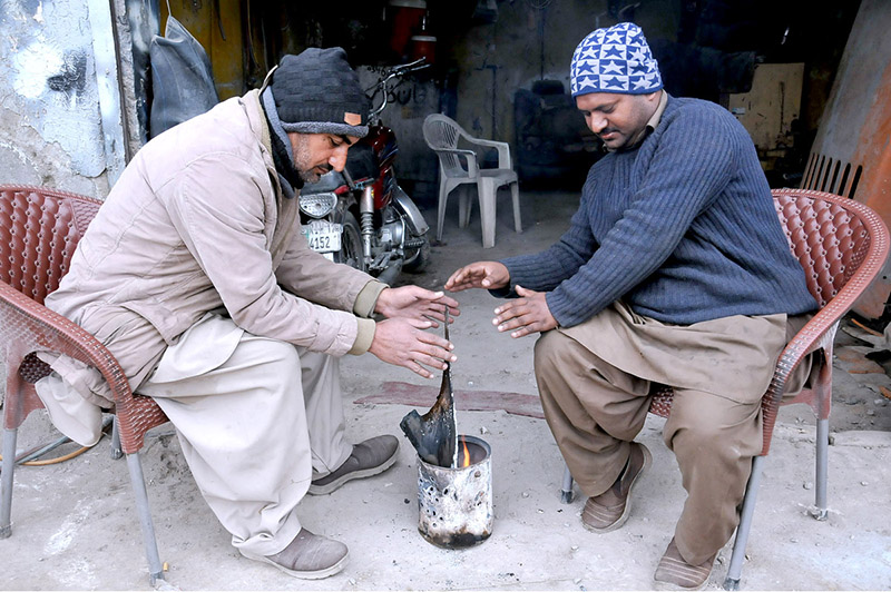 Mechanics sit around the fire to warm their hands as the temperature drops due to rain in the city