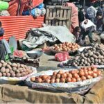 Two young vendors busy with cell phone while waiting for customers to sell potatoes and onion at Fruit and Vegetable Market.