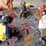 Women along with children busy in making flower bouquet for selling while sitting at roadside.
