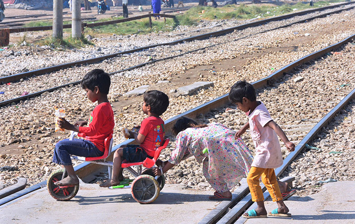 Children enjoy riding toy bicycle while crossing railway track near railway station.