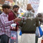 A vendor making bubble while displaying bubble making gun to attract the customers in a local market.