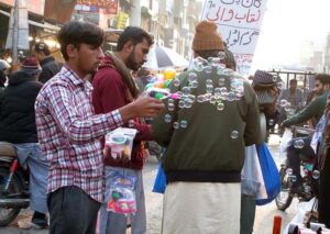 A vendor making bubble while displaying bubble making gun to attract the customers in a local market. 