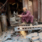 A blacksmith is busy at his workplace cutting large pieces of iron and making molds.