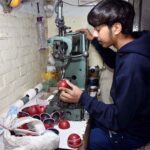 A worker is stitching a cricket ball at manufacturing unit