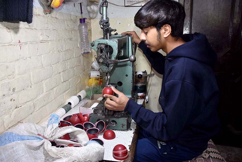A worker is stitching a cricket ball at manufacturing unit