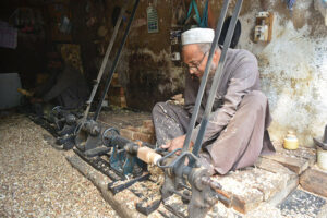 A carpenter busy in making part of a traditional bed (charpai) at his workplace.