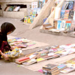 A woman selecting and purchasing old books from a roadside stall at Mall Road