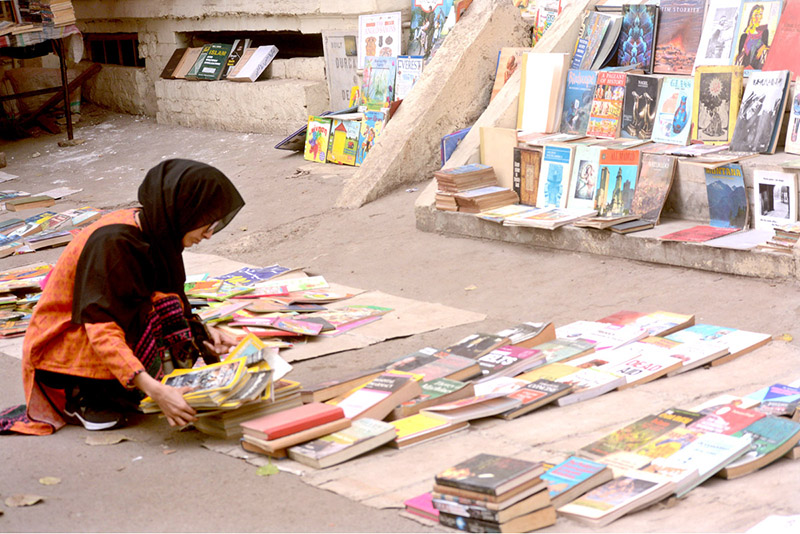 A woman selecting and purchasing old books from a roadside stall at Mall Road
