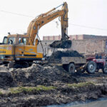 A crane driver loading garbage on a tractor trolly after cleaning a canal with the help of heavy machinery.