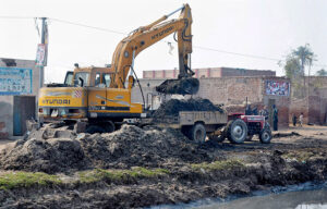 A crane driver loading garbage on a tractor trolly after cleaning a canal with the help of heavy machinery. 