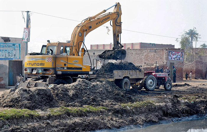 A crane driver loading garbage on a tractor trolly after cleaning a canal with the help of heavy machinery.