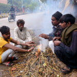 People sitting around the fire to keep them warm in a chilled weather during morning time