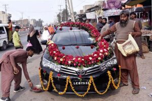 Workers decorating car with flowers for marriage ceremony.
