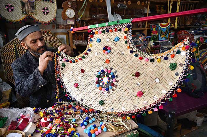 An artisan decorates hand fan at his workplace at Dabgari area.