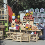 A vendor is busy arranging and displaying bird cages and other items to attract customers at his roadside setup.