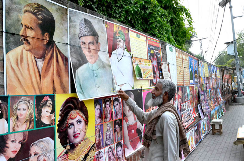 An elderly man is decorating printed pictures on the wall to earn a living for children in the Provincial Capital city