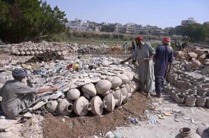 A worker woman paints clay-made pitcher at her work place near Jamshoro Road.