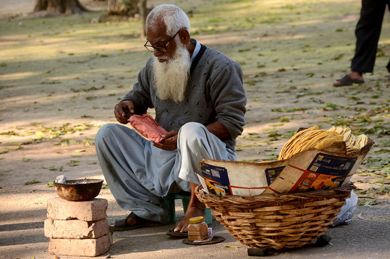An elderly person is selling the traditional food item paapar to the customers on his roadside setup