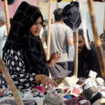 A woman buying used shoes at a roadside stall.