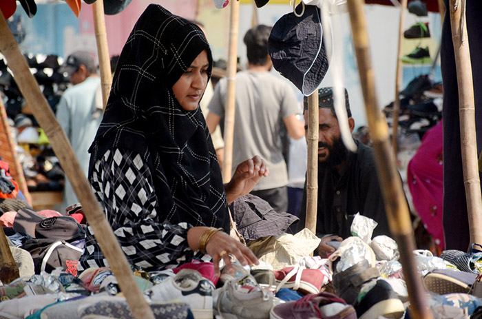 A woman buying used shoes at a roadside stall.