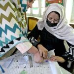 Women showing their identity card while standing in queue to cast their vote in polling station during General Election-2024