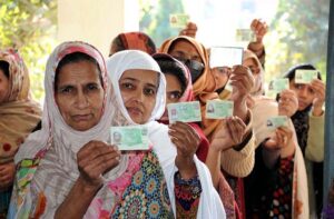 Polling officer marks the thumb of a woman voter before issuing ballot paper at a polling station during the General Election-2024.