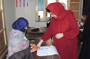 Polling officer marks the thumb of a woman voter before issuing ballot paper at a polling station during the General Election-2024.