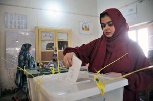 Polling officer marks the thumb of a woman voter before issuing ballot paper at a polling station during the General Election-2024.