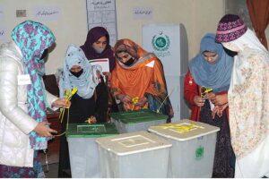 Polling officer marks the thumb of a woman voter before issuing ballot paper at a polling station during the General Election-2024.