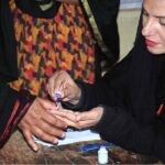 Polling officer marks the thumb of a woman voter before issuing ballot paper at a polling station during the General Election-2024.