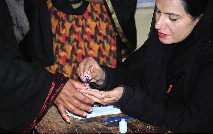 Polling officer marks the thumb of a woman voter before issuing ballot paper at a polling station during the General Election-2024.