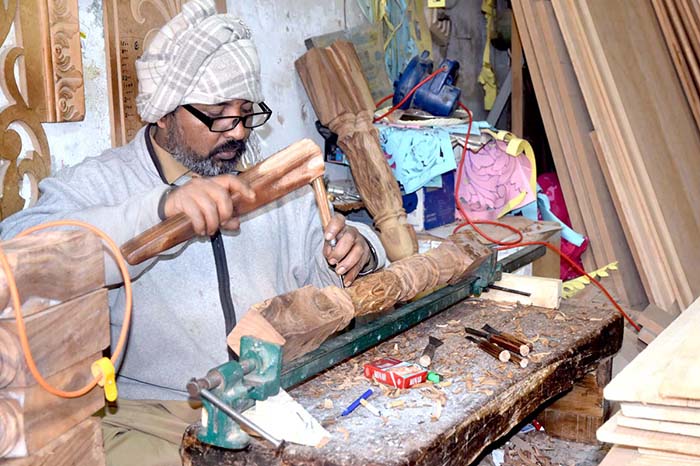 A carpenter making wooden furniture at his setup on Said Pur Road.