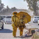 A brother and a sister wearing golden dresses waiting for people to give them charity at Chak Shahzad Road.