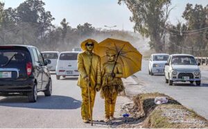A brother and a sister wearing golden dresses waiting for people to give them charity at Chak Shahzad Road.