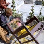 An aged man is netting a chair to earn for livelihood near Azadi chowk.