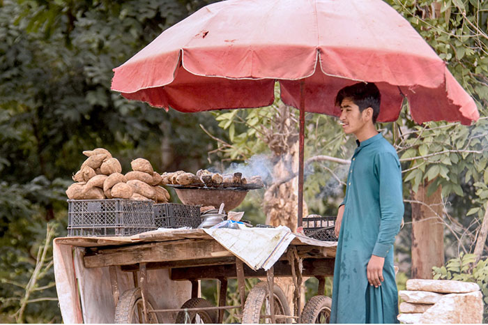 A street vendor displaying sweet potatoes to attract customers at his roadside setup on Chak Shahzad Road.