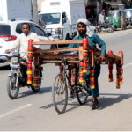 A street vendor selling a frame of a traditional bed (charpai) while shuttling on the road