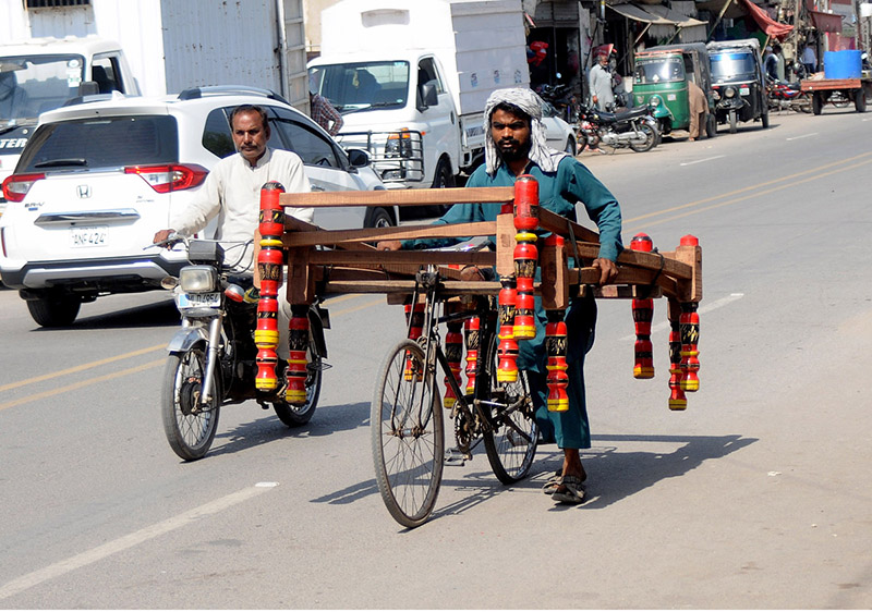 A street vendor selling a frame of a traditional bed (charpai) while shuttling on the road