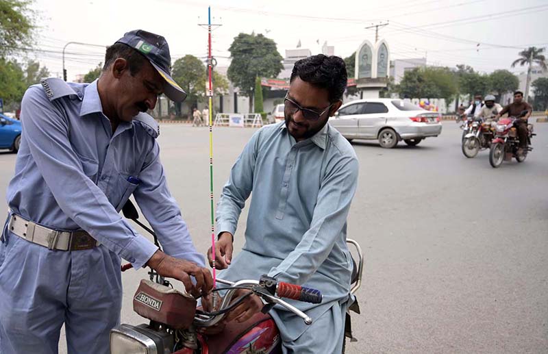 A traffic police personnel installing a kite string protector on a motorcycle for safety from a stray kite string at Club Chowk.