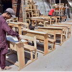 A carpenter busy in giving final touches of school desks after preparing at his workplace.