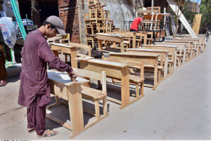 A carpenter busy in giving final touches of school desks after preparing at his workplace.