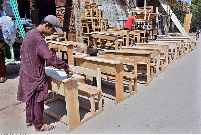 A carpenter busy in giving final touches of school desks after preparing at his workplace.