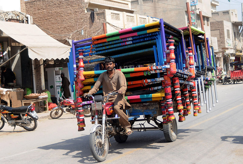 A tricycle holder on the way loaded with traditional beds (Charpai) heading toward his destination