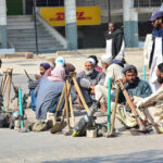 Labourers along with their tools sitting on roadside waiting for clients to be hired for work at Latifabad