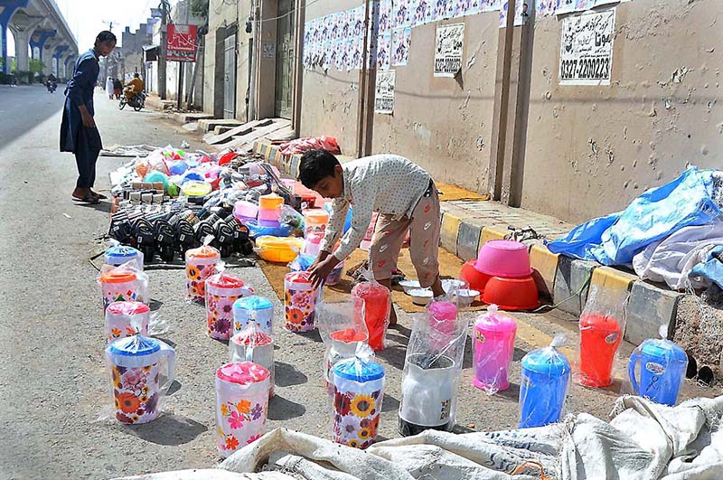 A boy displaying plastic jugs to attract customers at his roadside setup.