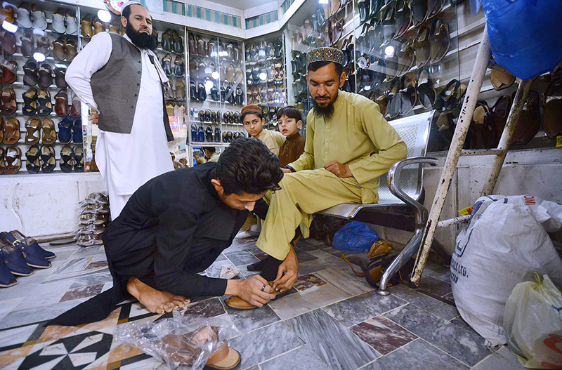 Customer selecting and purchasing traditional shoes (Peshawari Chappal) from a shopkeeper in preparation connection with upcoming Eid-ul-Fitar