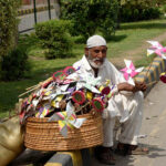 An elderly man is sitting on the footpath selling traditional Toys for Children at Shah Jamal road
